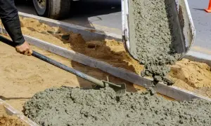 Robotnik rozprowadza łopatą świeży cement z wodą bez piasku, wylewany z betoniarki na budowie.