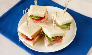 Quattro tramezzini quadrati con prosciutto, lattuga e pomodoro, perfetti per idee gusti tramezzini veloci e sfiziosi.