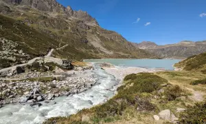 Berglandschaft mit türkisfarbenem Wasser des Silvretta Stausees, der von einem Fluss gespeist wird. Wanderweg schlängelt sich den Hang hinauf.