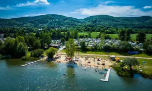 Jezioro Bielawskie oferuje mnóstwo atrakcji: plażę z kąpiącymi się ludźmi, molo, a w tle kemping i zielone wzgórza.