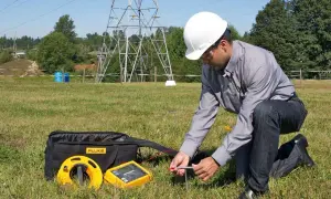 Technicien en plein air vérifiant la valeur prise de terre d'une maison, près d'un pylône électrique.