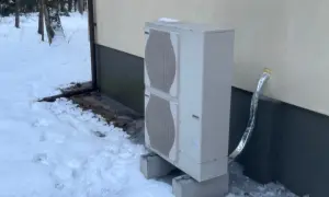Jednostka zewnętrzna pompy ciepła stoi na betonowych podstawach w zasypanym śniegiem ogrodzie. Czy pompa ciepła jest głośna? Zimą, gdy wszystko wokół jest ciche, można to sprawdzić.