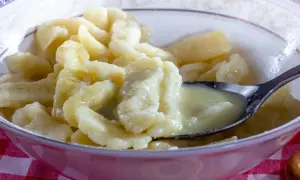 Miska pełna pysznych, domowych klusek kładzionych polanych śmietaną. Łyżeczka nabiera porcję tych delikatnych kluseczek.