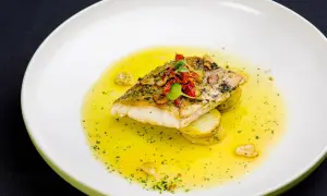 Filet ryby na plastrach ziemniaków, polany bogatym, złocistym sosem maślano cytrynowym, ozdobiony ziołami i suszonymi pomidorami.