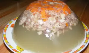 Pyszna galareta z golonki, z kawałkami mięsa i marchewki, w przezroczystej, galaretowatej masie.