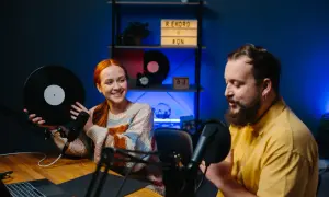 Coppia discute di come fare un podcast, lei tiene un vinile, lui parla al microfono.