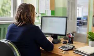 Donna al computer, con calcolatrice e monete sul tavolo, per l'emissione busta paga e accredito stipendio.