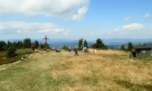 Wielka racza szlaki to widok na szczyt z krzyżem i ludźmi odpoczywającymi na trawie.