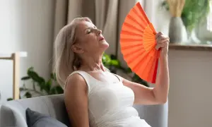 Kobieta w wieku około 50 lat wachluje się, doświadczając uderzeń gorąca. To częsty objaw menopauzy w jakim wieku się pojawia.