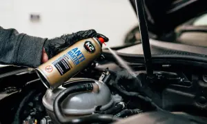Ręka w rękawiczce rozpyla środek "Anti Marten" w komorze silnika, chroniąc auto przed kunami.