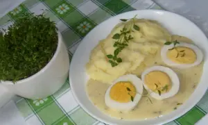 Pyszne ziemniaki puree z jajkami w sosie chrzanowym na ciepło, udekorowane gałązkami ziół. Obok doniczka ze świeżą rzeżuchą.