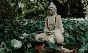 Kamienna figura Buddy w pozycji medytacyjnej, otoczona liśćmi lotosu.