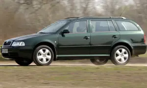 Zielona Skoda Octavia 2010 kombi jedzie po polnej drodze, unosząc kurz.