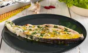 Un succulento pesce spada al forno, condito con erbe aromatiche e olio d'oliva, servito su un piatto scuro.