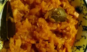 Pyszny bigos ze słodkiej kapusty, z dodatkiem liści laurowych, w żółtej misce z ozdobnym wzorem.