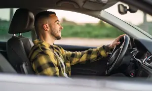Joven sonriente conduce con las manos en el volante, promoviendo la seguridad al volante.