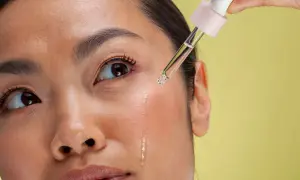 Kropla serum z pipetki spada na policzek kobiety. To może być retinol, który pomaga w pielęgnacji skóry.