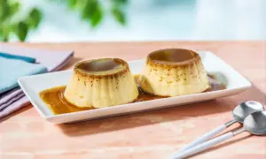 Zwei köstliche flan caramel Desserts auf einem weißen Teller, mit flüssiger Karamellsauce übergossen. Löffel liegen daneben.