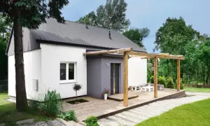 Drewniany taras połączony z wejściem do domu, z pergolą i meblami ogrodowymi.