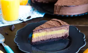 Pyszny tort pomarańczowo czekoladowy z warstwami musu i owocową galaretką, posypany kakao. Obok szklanka soku pomarańczowego.