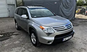 Srebrny Suzuki XL7 zaparkowany przed szarym namiotem.