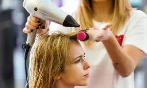 Fryzjerka suszy włosy klientce suszarką i okrągłą szczotką, pokazując, jak suszyć włosy dla pięknej fryzury.