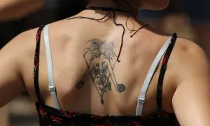 Tatuaz znak zodiaku na plecach kobiety, przedstawiający postać z kwiatami w geometrycznej ramie.