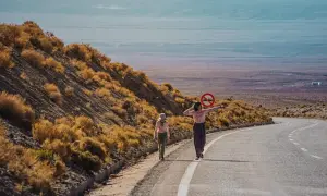Dwie dziewczynki w kolorowych ubraniach idą pustynią Atacama. Jedna z nich trzyma znak zakazu ruchu.