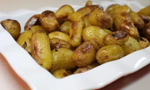 Un plat blanc rempli de pommes de terre nouvelles rôties, dorées et appétissantes.