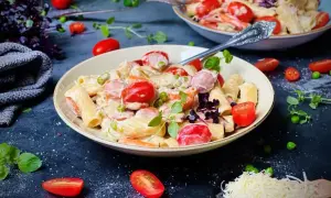 Cremige Pasta mit Würstchen, Erbsen und Kirschtomaten – ein köstliches One-Pot-Gericht, garniert mit frischen Kräutern.