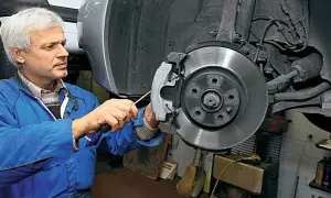 Mechanik w niebieskim kombinezonie pracuje nad tarczą hamulcową samochodu, dbając o sprawność układu hamulcowego.