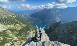 Dwóch wspinaczy na szczycie, z widokiem na Tatry i Morskie Oko. Mnich tatrzański w tle.