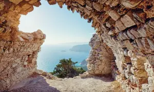 Blick durch eine Felsenruine auf das azurblaue Meer. Ein absolutes Rhodos Must See für Geschichts- und Naturliebhaber.