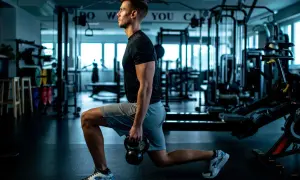 Mann macht Ausfallschritte mit Kettlebell im Fitnessstudio. Verschiedene Ausfallschritte Varianten trainieren Beine und Po.