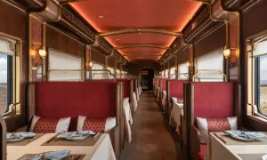Lyxig tågvagn med röda säten och dukade bord, redo för fantastiska tågresor genom ett ökenlandskap.