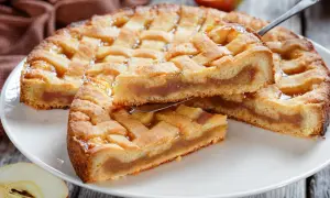 Ein goldbrauner Kuchen mit Gittermuster, gefüllt mit süßem Apfelmus. Ein Stück wird gerade herausgehoben.