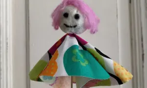 Eine selbstgemachte Puppe mit pinker Wolle als Haar und buntem Stoffkleid. Perfekt zum Filzen mit Kindern.