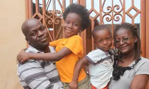 Famille souriante devant une fenêtre ornée. L'homme porte un enfant, la fille étreint son père. L'origine d'Anthony Samama est peut-être liée à cette joie familiale.