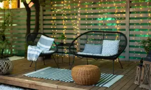 Gemütliche Terrasse gestalten mit wenig Geld: Zwei schwarze Korbsessel, ein Sofa, ein Teppich und Lichterketten schaffen eine einladende Atmosphäre.