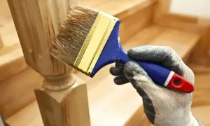 Ręka w rękawicy maluje pędzlem drewniany słupek schodów.