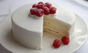 En vacker white lady tårta med fluffig grädde och färska hallon. En bit är bortskuren och visar de läckra lagren.