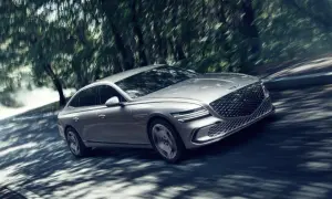Silver Genesis G80 Sverige glider genom en skogsväg, skuggor dansar över bilen.