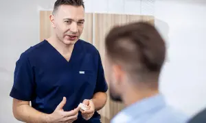 Dentysta w granatowym uniformie pokazuje pacjentowi model szczęki.