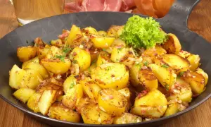 Goldbraune Bratkartoffeln mit Speck und Zwiebeln, garniert mit Petersilie. Ein klassisches Bratkartoffeln Rezept, serviert in einer Eisenpfanne.