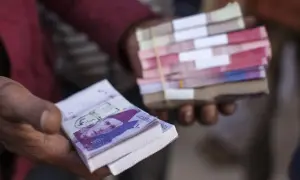 Dłonie trzymają stosy banknotów. W jednej dłoni widać wyraźnie banknot z portretem, to waluta Pakistanu.