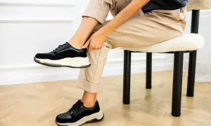 Kobieta w beżowych spodniach i czarnych sneakersach pokazuje, jak szybko wysuszyć buty.