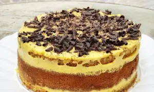 Torta pazientina a strati, con crema gialla e riccioli di cioccolato fondente in cima.