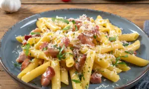 Penne rigate z chrupiącym boczkiem, posypane parmezanem i natką pietruszki. Pyszne makaron z boczkiem na talerzu.