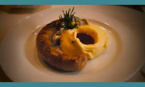 Une saucisse grillée, courbée sur une purée onctueuse, garnie de romarin et de sauce. Un plat réconfortant de saucisse purée.
