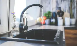 Ein Wasserhahn tropft in eine Spüle. Ein kleiner Strauß Blumen steht daneben. Dies könnte ein Hinweis auf den Kaltwasserverbrauch pro Person sein.